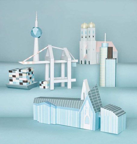 Papiermodelle bekannter Gebäude, darunter Fernsehturm und Kirchen, auf blauem Hintergrund.